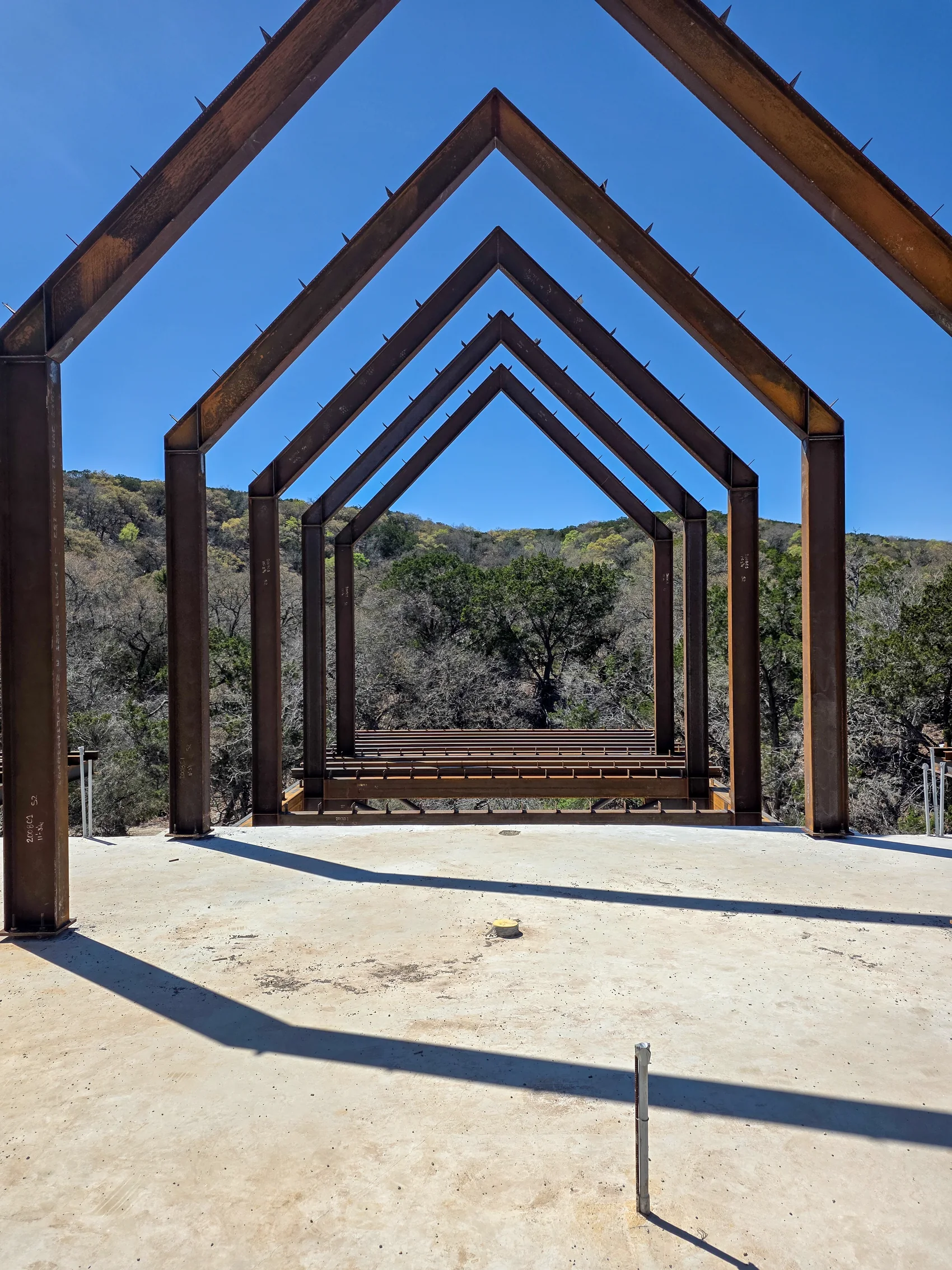 Arroyo Verde steel gable frames aligned toward the Hill Country trees