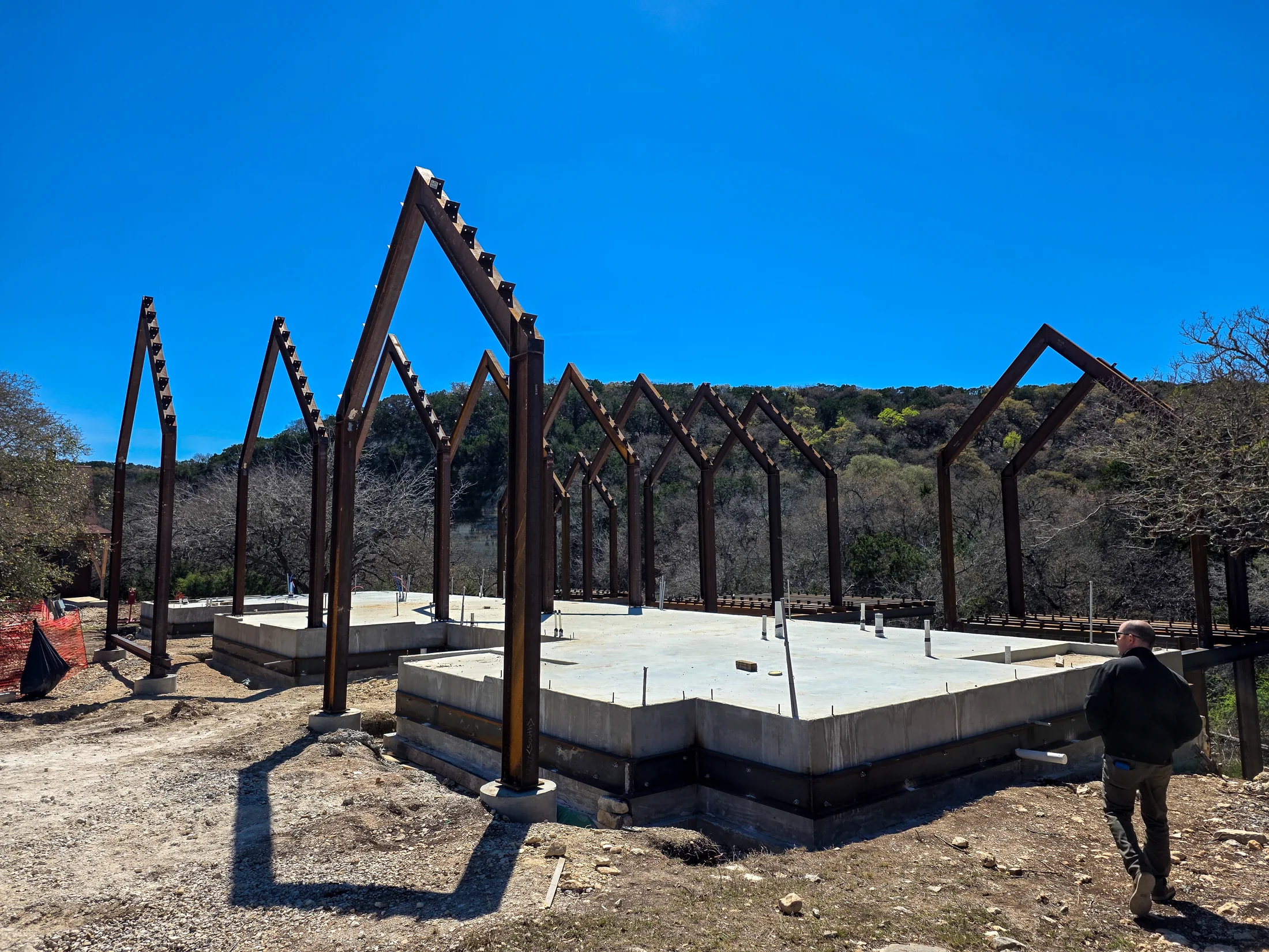 Arroyo Verde steel gable frames under construction against a Hill Country bluff